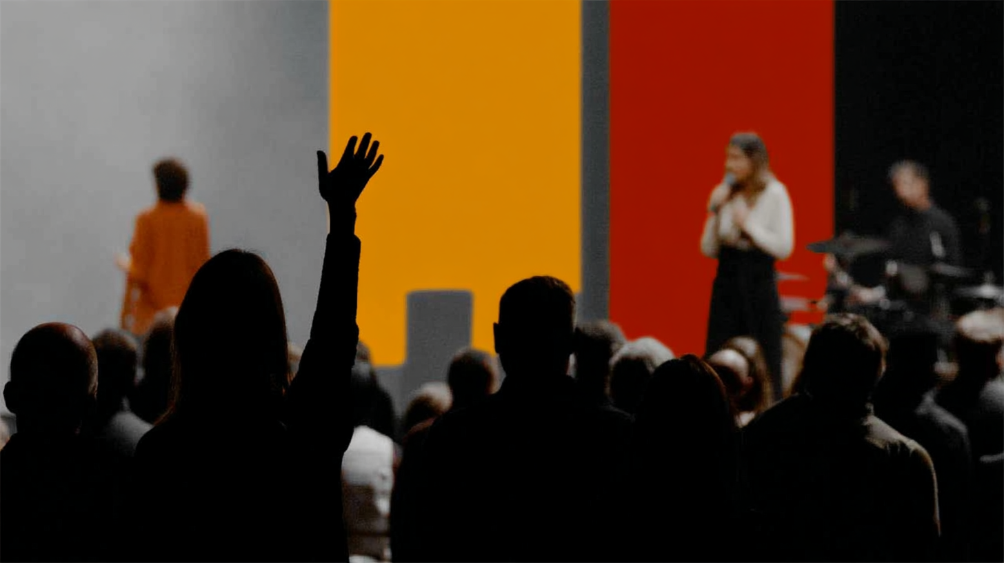 People worshipping in a modern church setting, with a raised hand in the foreground, vibrant colored backdrop, and a worship leader speaking.