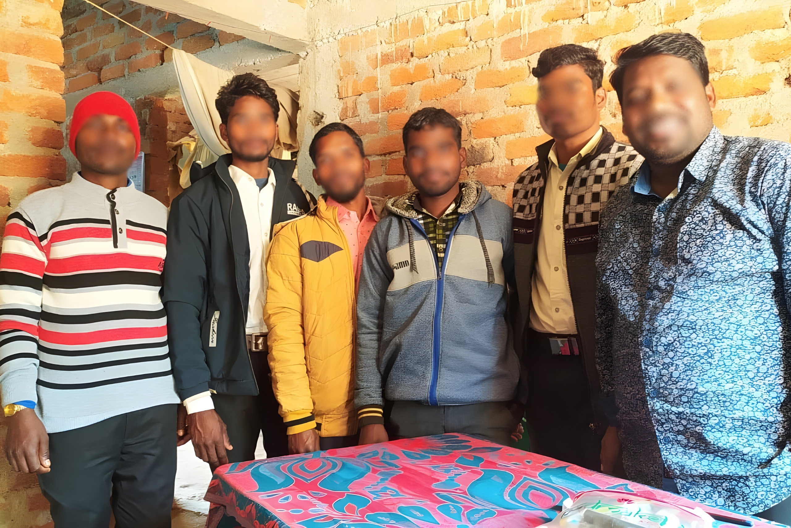 Group of six men in a rustic indoor setting, showcasing community support and collaboration for the Amaravati Pathway ministry initiative, with a colorful tablecloth symbolizing hope and transformation.