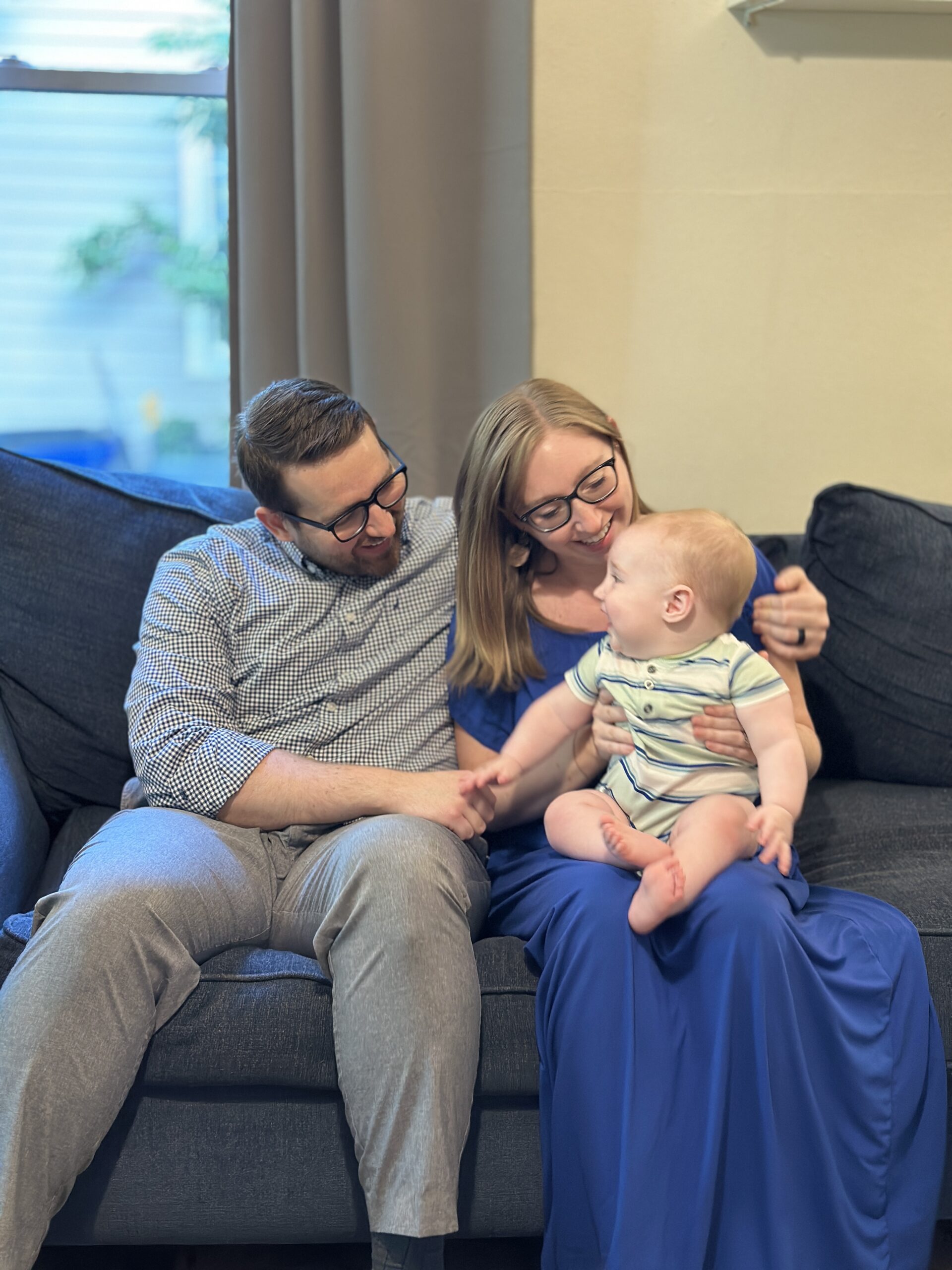 Family interacting on a couch, smiling and engaging with a baby, highlighting connection and joy in a home setting.