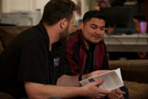 Two men engaged in a discussion, one holding a book, in a casual setting, illustrating mentorship and leadership training for church planting initiatives.