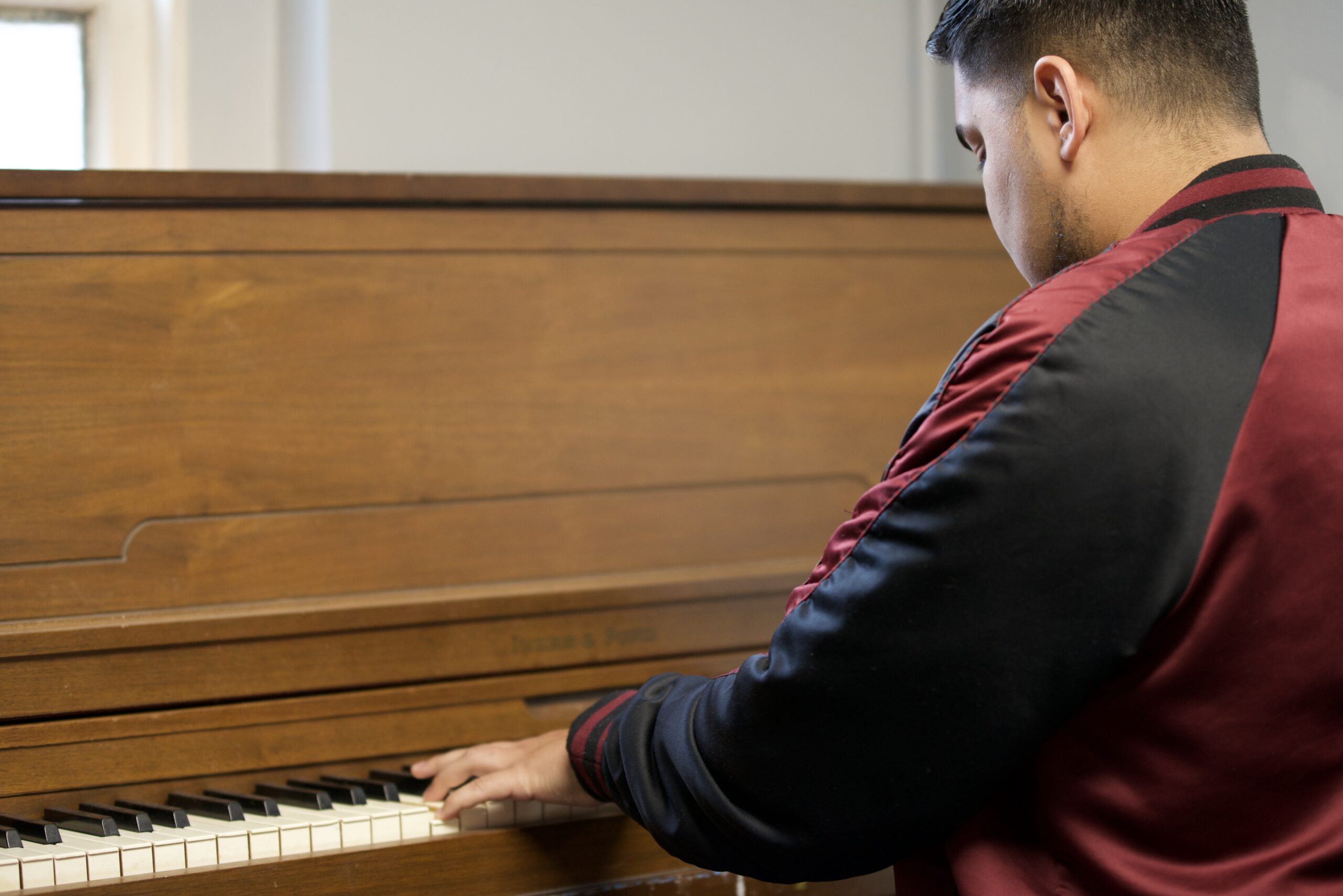 Young man playing piano, wearing a black and red jacket, in a supportive church environment promoting community and worship.