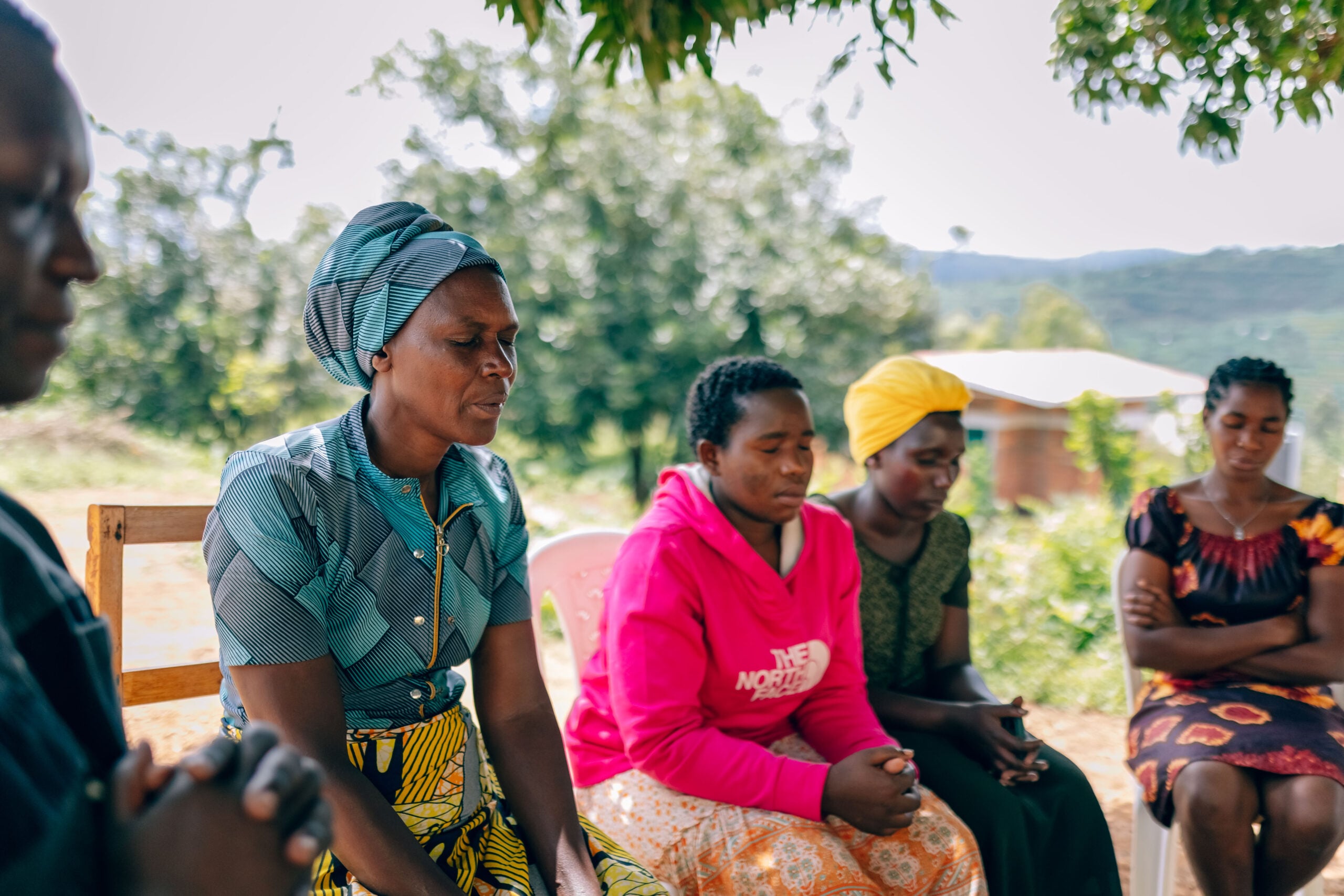 Women praying together in a rural setting, reflecting community support and discipleship in Rusasa, Rwanda, as part of a decentralized church initiative.