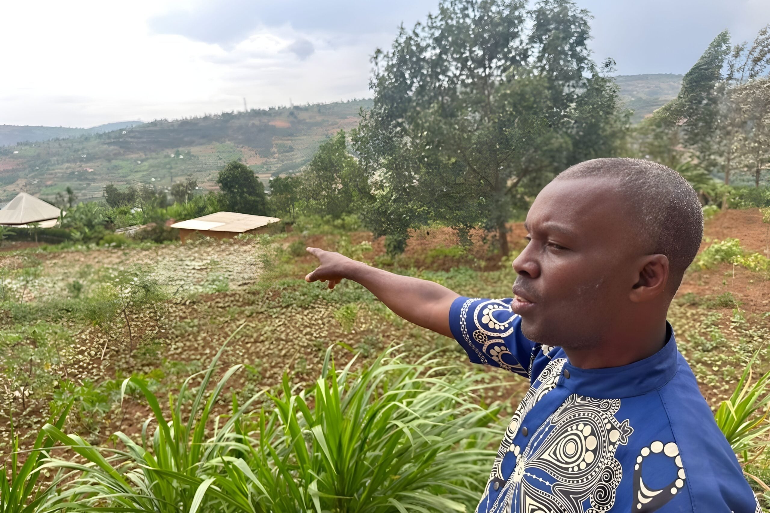 Pastor Jean pointing towards the hills where house churches are forming, surrounded by greenery and a rural landscape, symbolizing community transformation and church revival efforts in Rwanda.