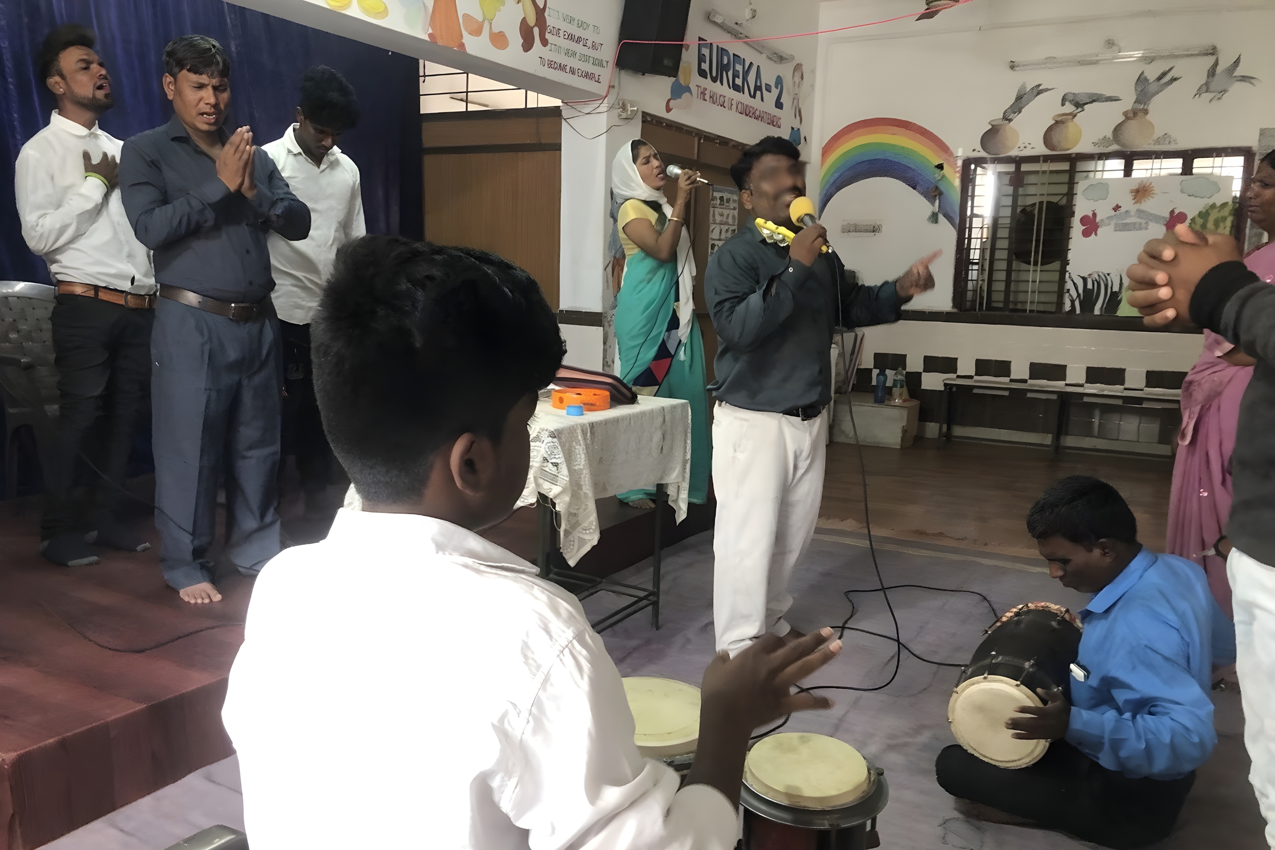 Group of worshippers engaged in a church service, with Pastor P.A. speaking into a microphone, surrounded by attendees praying and playing percussion instruments, emphasizing community and spiritual transformation in Amaravati.