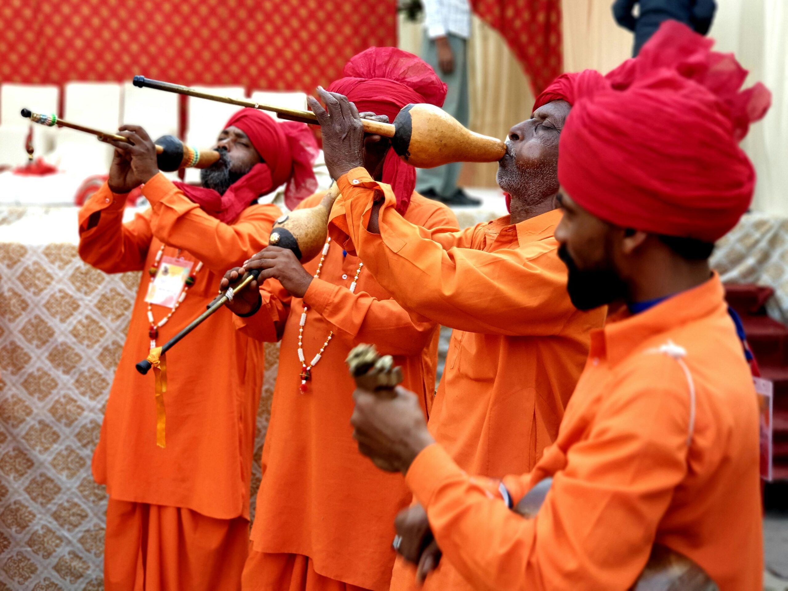 Musicians in orange attire playing traditional instruments at a cultural event, emphasizing community and support in ministry.