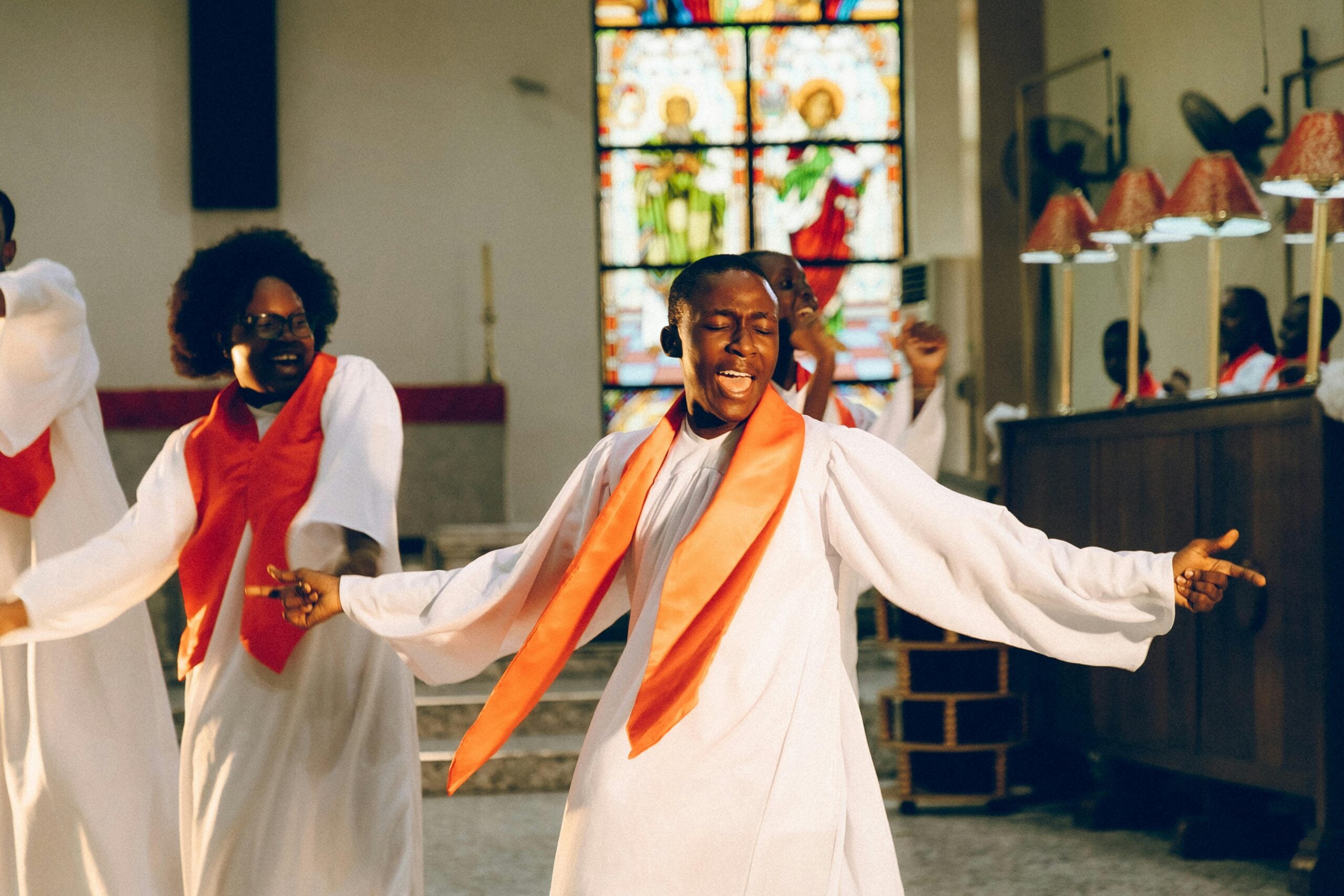 Worshippers in white robes with orange stoles joyfully dancing in a church setting, symbolizing a vibrant, Spirit-led movement of believers in Rwanda.