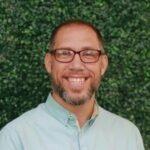 Daniel Mackey, Youth Pastor at Multiply Family of Churches, smiling against a green backdrop, embodying community and faith in the context of grace and identity in Christ.
