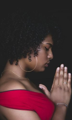 Young woman in red dress praying with hands clasped, embodying faith and community involvement for Multiply the Church initiatives.